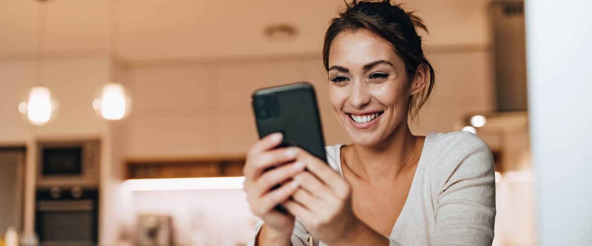 Woman wearing glasses is holding her phone with both hands and looking at it.